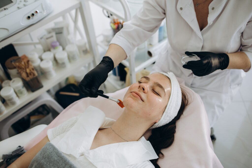 Woman receiving a professional facial peel in a clinic treatment room, clinician applying peel with brush.
